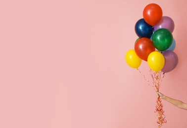 Photo of Woman holding bunch of bright balloons on color background, space for text. Celebration time