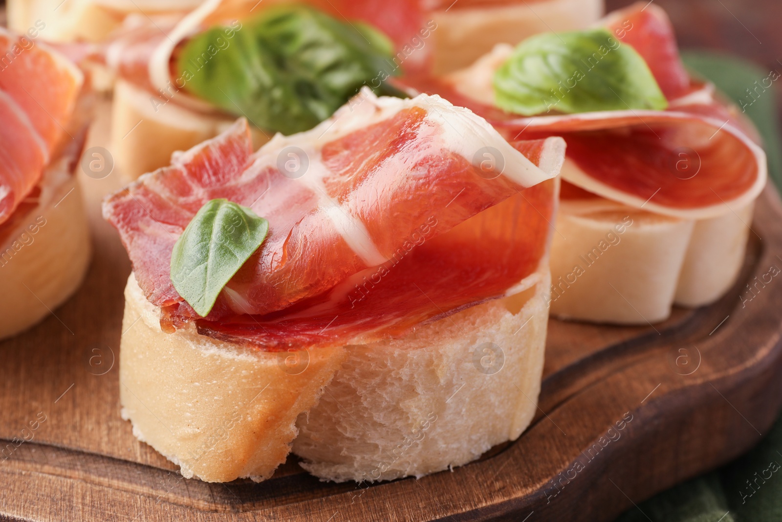 Photo of Tasty sandwiches with cured ham and basil leaves on wooden board, closeup