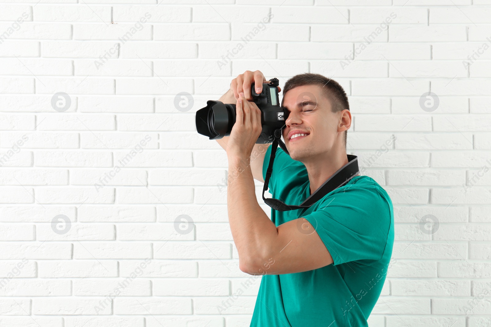 Photo of Young professional photographer taking picture near brick wall. Space for text