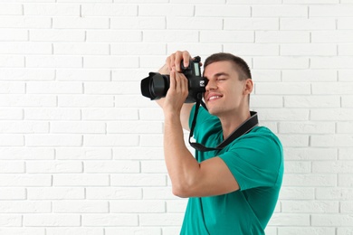 Young professional photographer taking picture near brick wall. Space for text