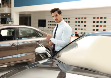 Young salesman near new car in modern dealership