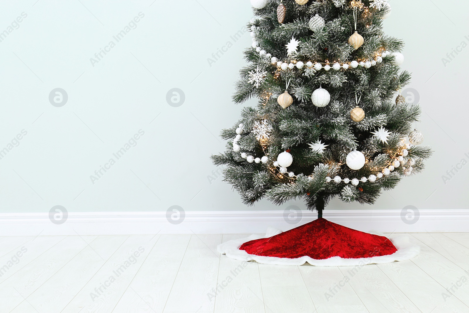 Photo of Decorated Christmas tree with red skirt indoors, space for text