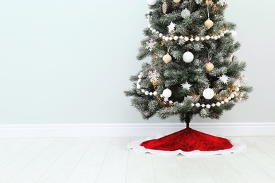 Decorated Christmas tree with red skirt indoors, space for text