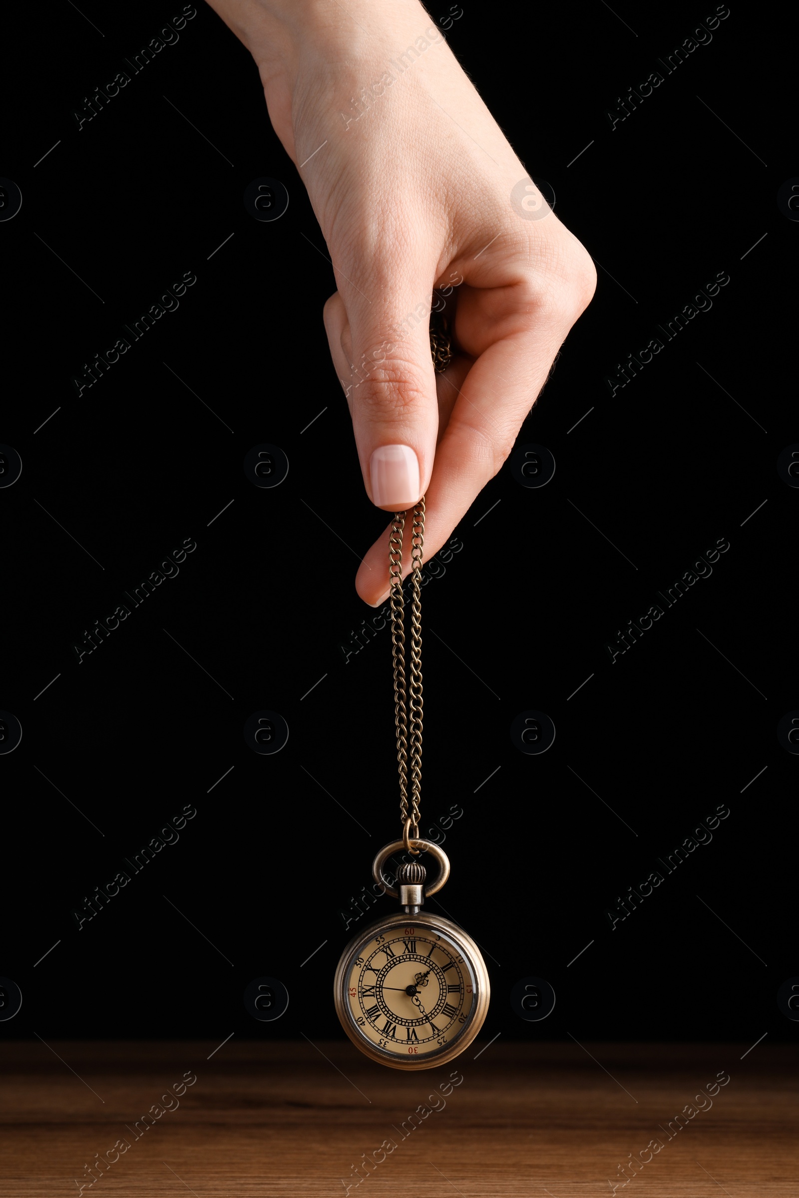 Photo of Psychotherapist with pendulum on black background, closeup. Hypnotherapy session