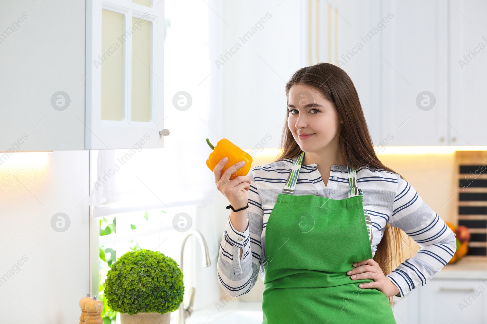 Photo of Young woman with apron and bell pepper in kitchen