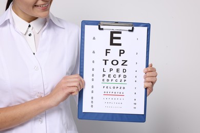 Photo of Ophthalmologist with vision test chart on light background, closeup