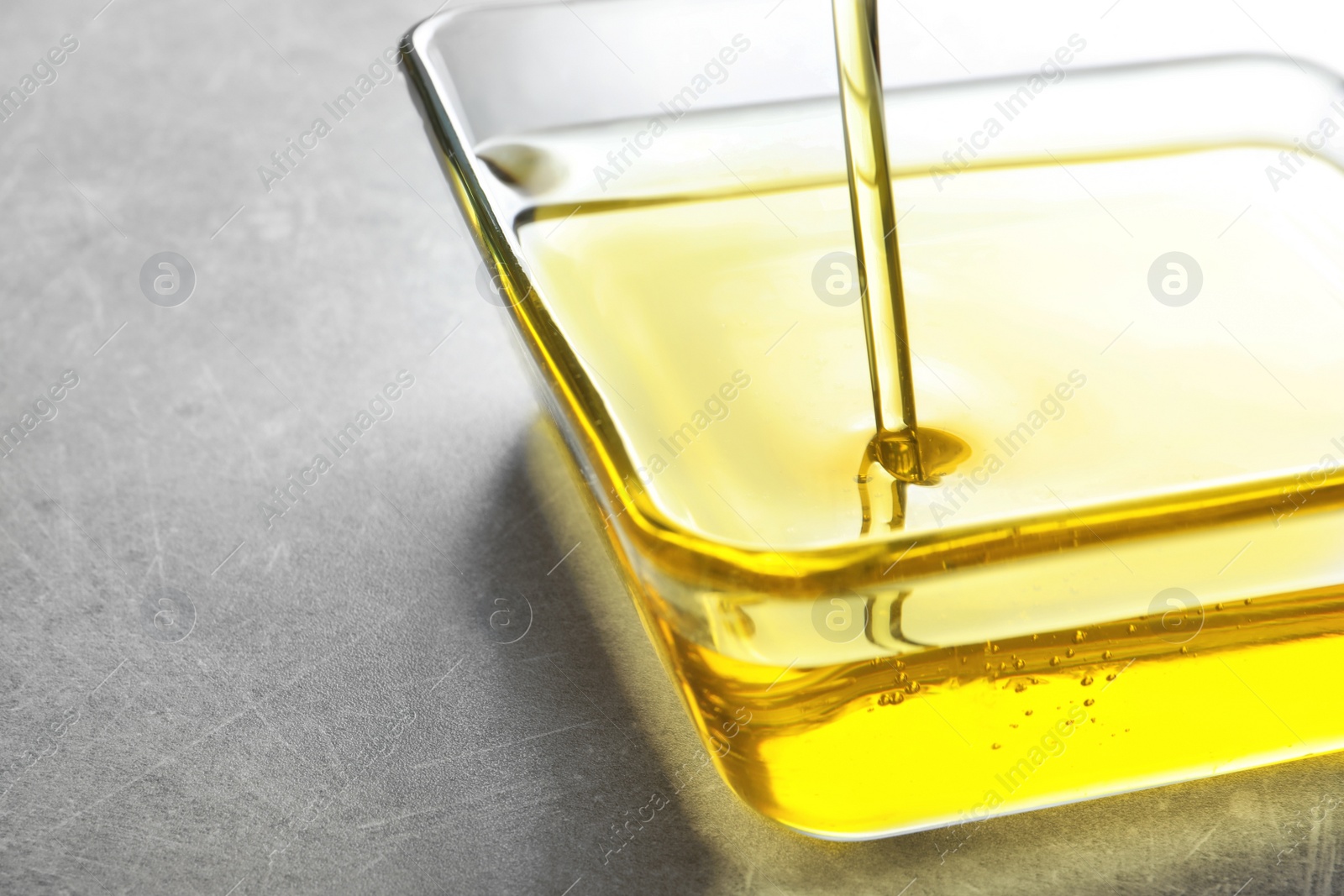 Photo of Pouring fresh olive oil into bowl on grey background, closeup