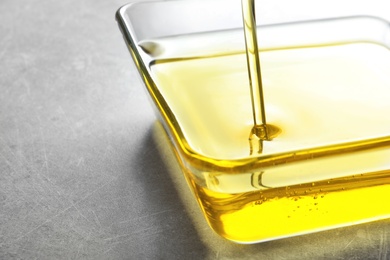 Pouring fresh olive oil into bowl on grey background, closeup