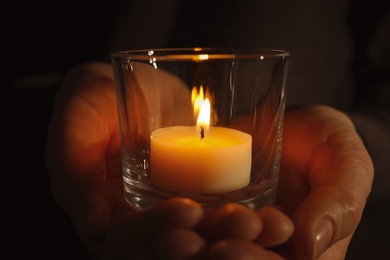 Photo of Young person holding burning candle in darkness, closeup