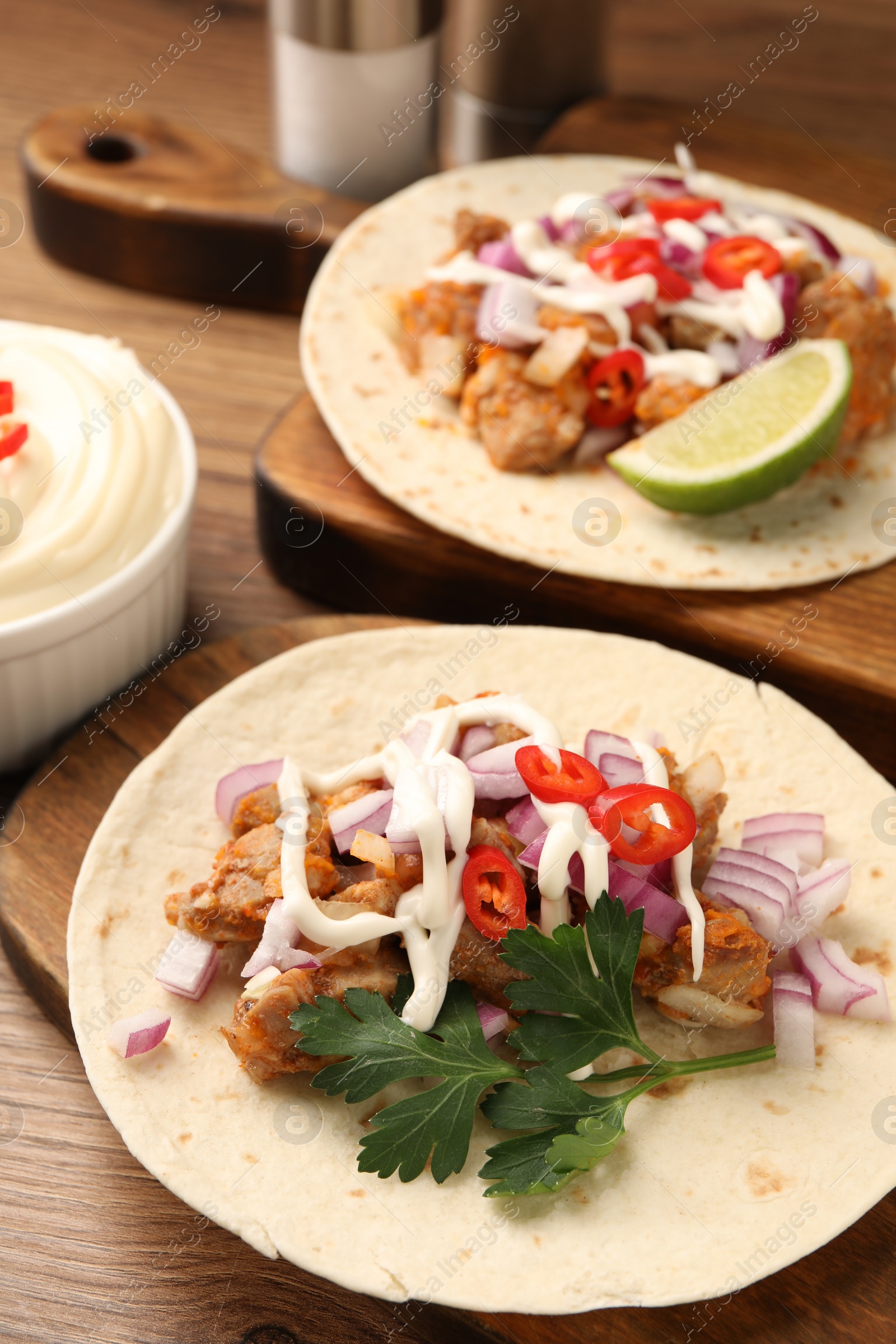 Photo of Delicious tacos with vegetables, meat and sauce on wooden table