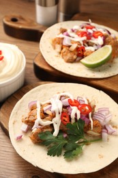 Delicious tacos with vegetables, meat and sauce on wooden table