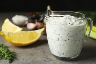 Photo of Glass jug of Tzatziki cucumber sauce with ingredients on table. Space for text