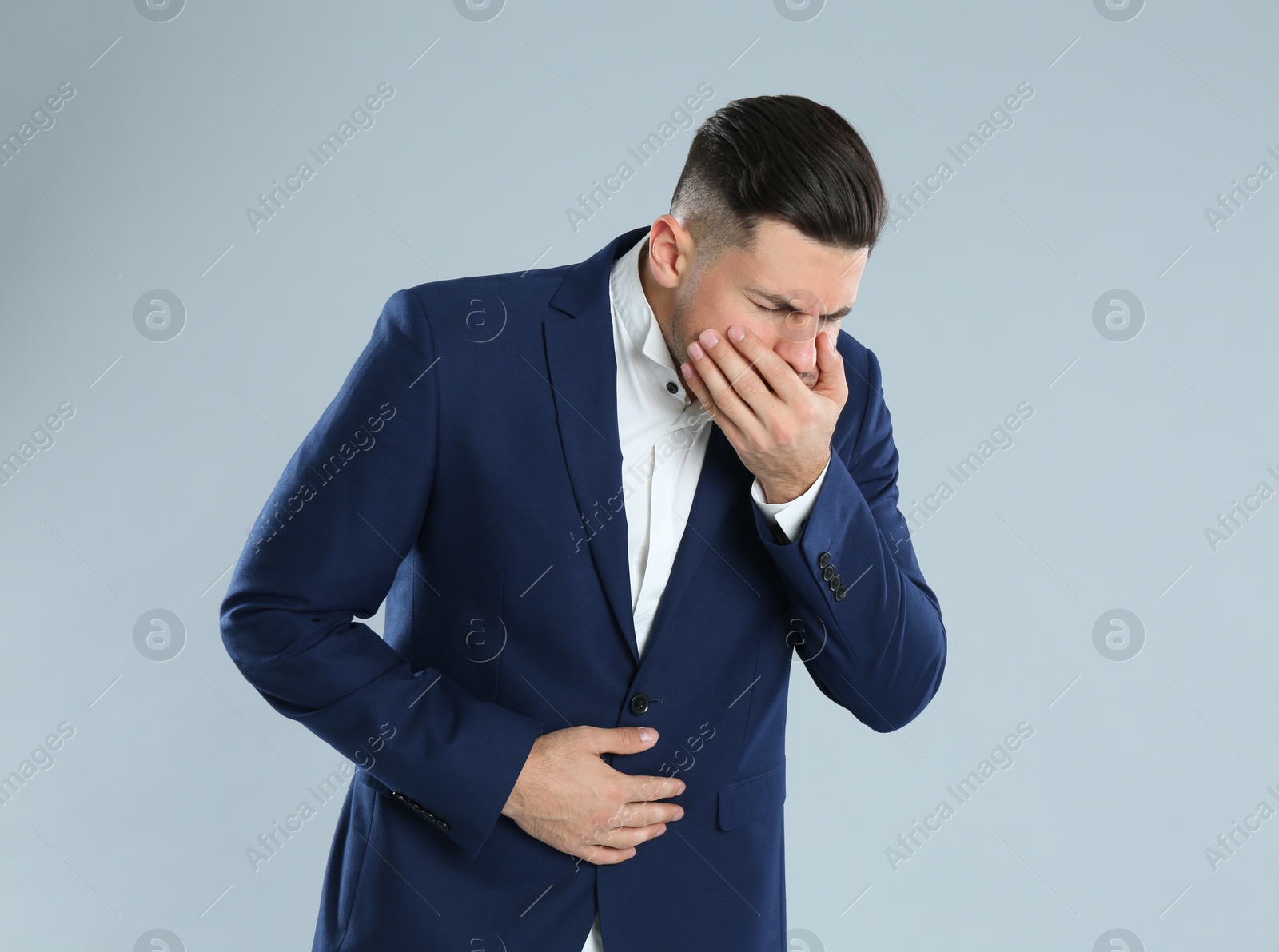 Photo of Man in office suit suffering from stomach ache and nausea on grey background. Food poisoning