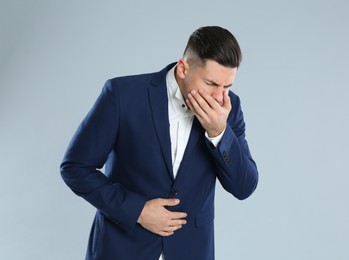Man in office suit suffering from stomach ache and nausea on grey background. Food poisoning
