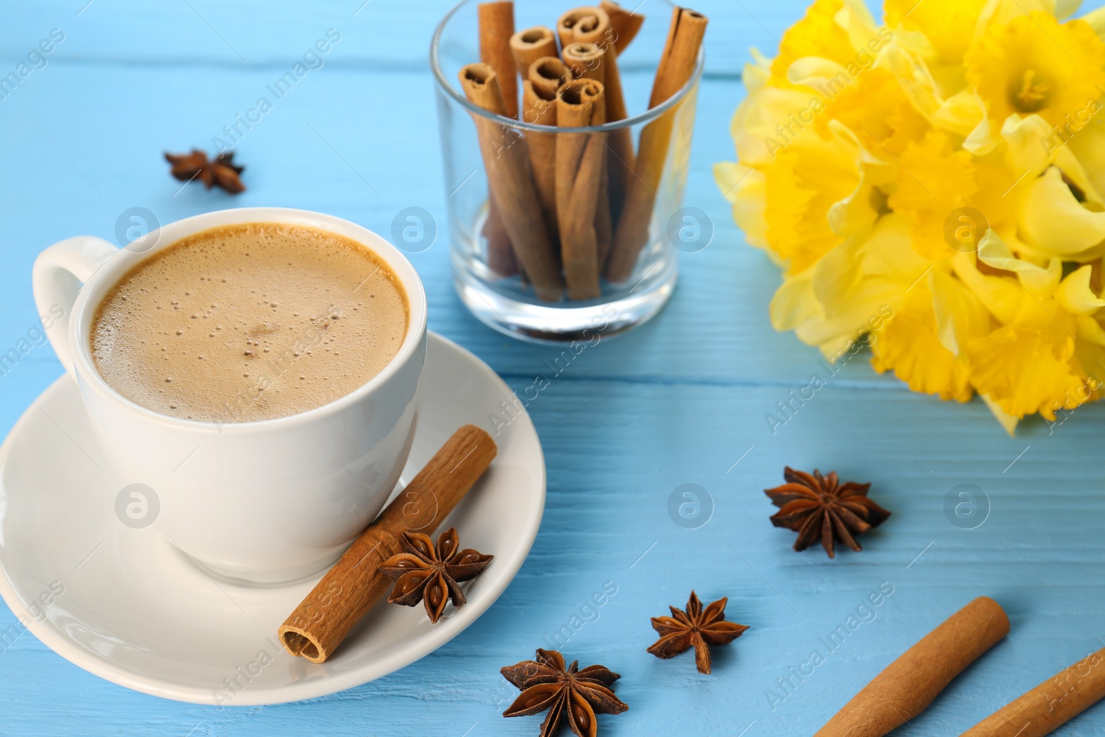 Photo of Cup of coffee, cinnamon, anise stars and beautiful yellow daffodils on light blue wooden table