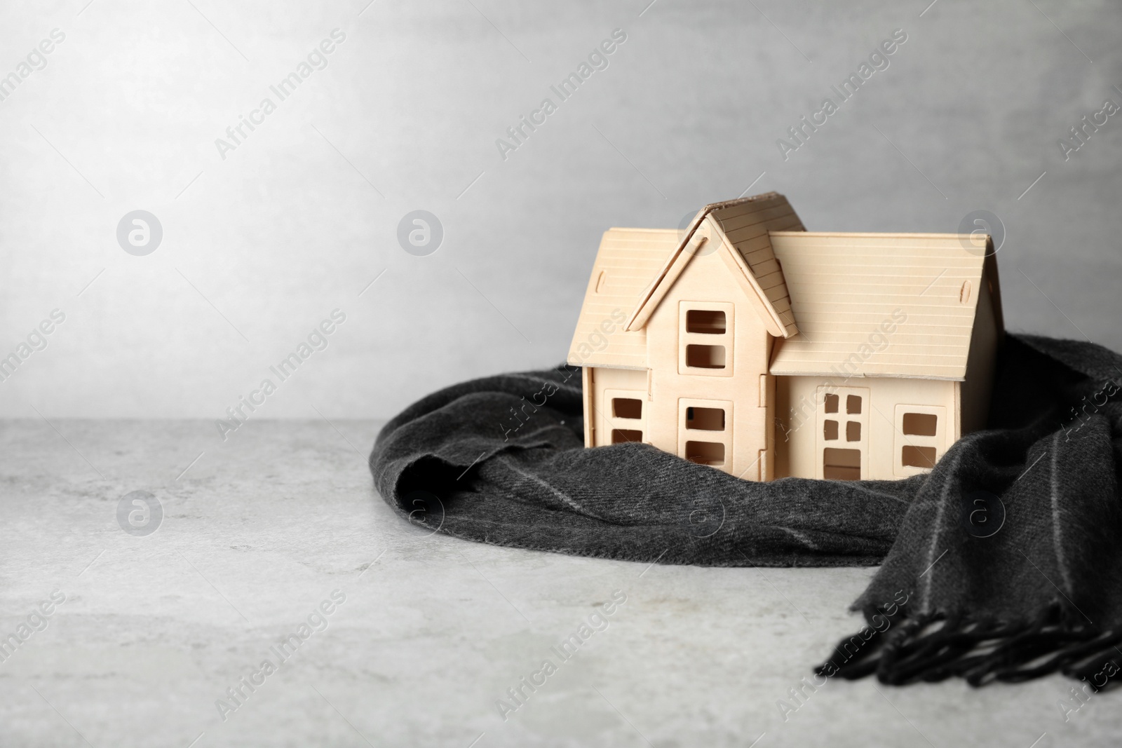 Photo of Wooden house model and scarf on light grey stone table, space for text. Heating efficiency