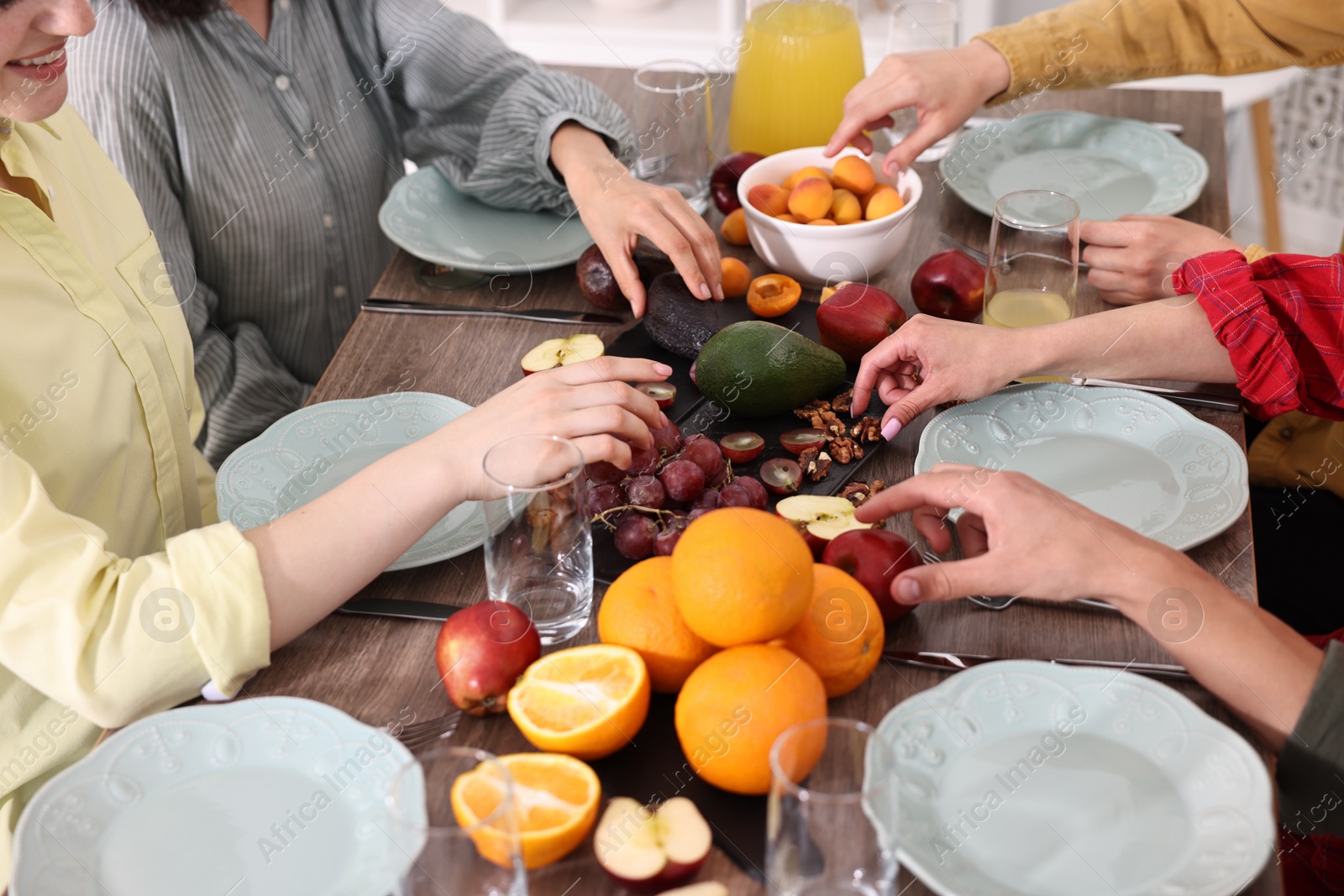 Photo of Vegetarian food. Friends eating fresh fruits at wooden table indoors, closeup