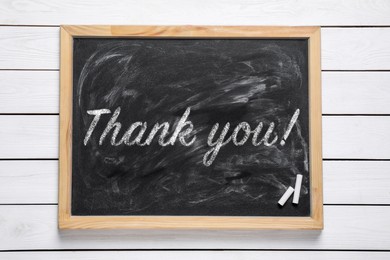 Image of Small blackboard with pieces of chalk and phrase Thank you! on white wooden table, top view