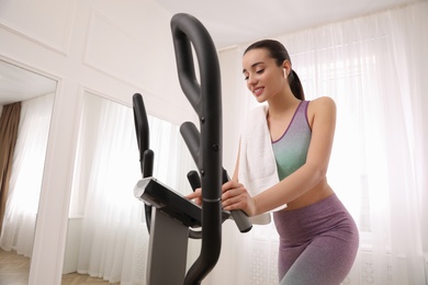 Photo of Woman with towel using modern elliptical machine at home