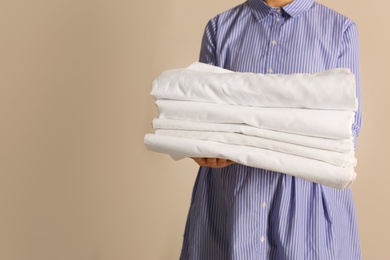Photo of Woman holding stack of clean bed linens on beige background. Space for text