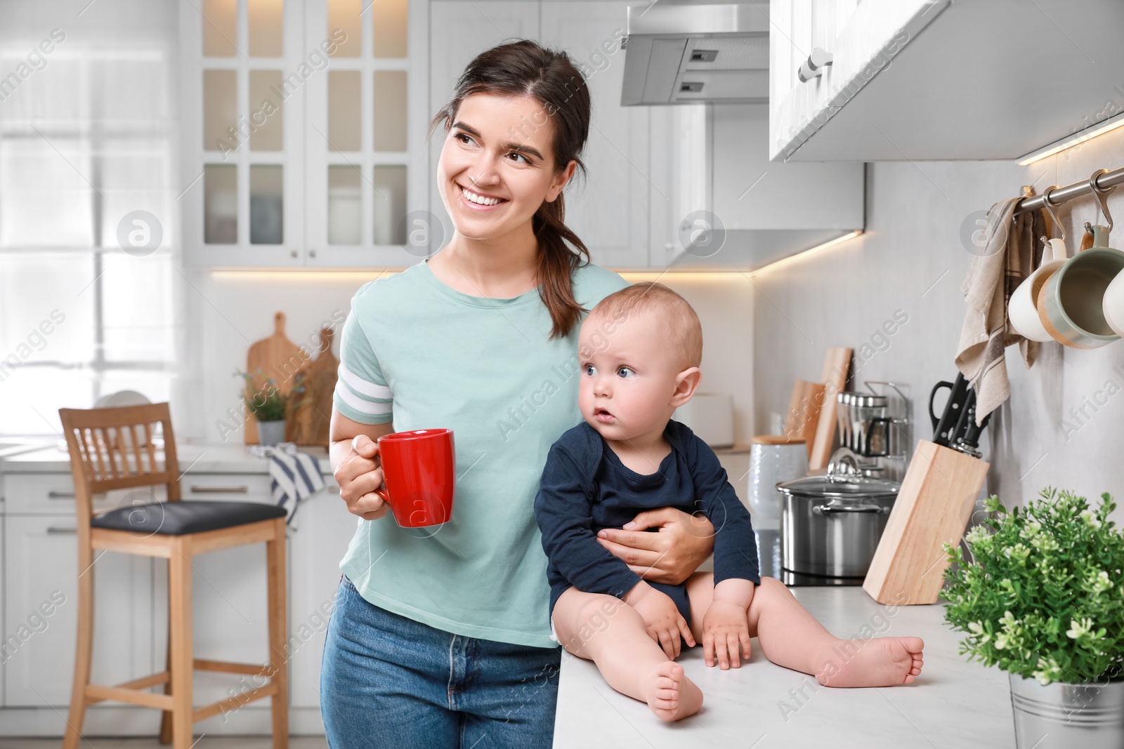 Photo of Happy young woman and her cute little baby spending time together in kitchen