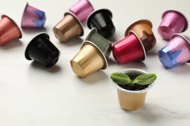 Photo of Coffee capsules and seedling on white marble table