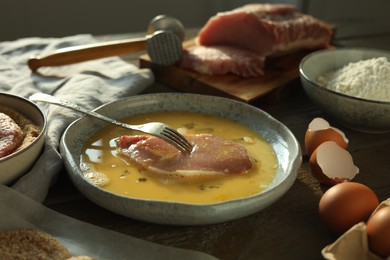 Photo of Cooking schnitzel. Raw pork chop in eggs, meat mallet and ingredients on wooden table