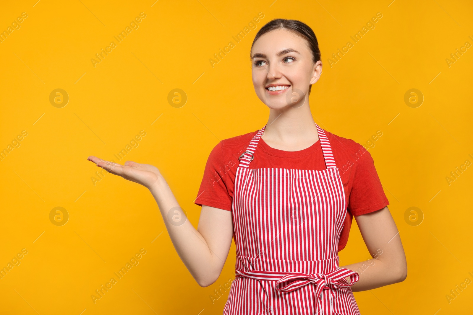 Photo of Beautiful young woman in clean striped apron on orange background