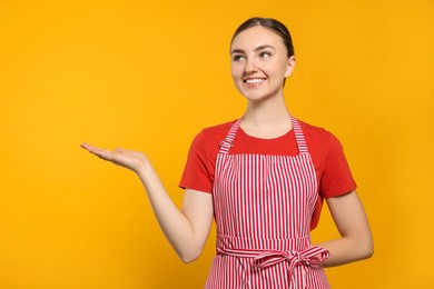 Beautiful young woman in clean striped apron on orange background