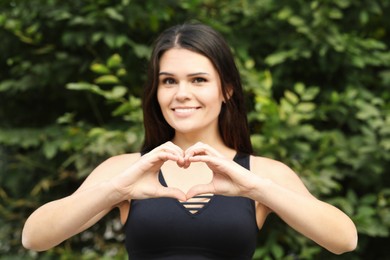 Photo of Happy young woman making heart shape with hands outdoors