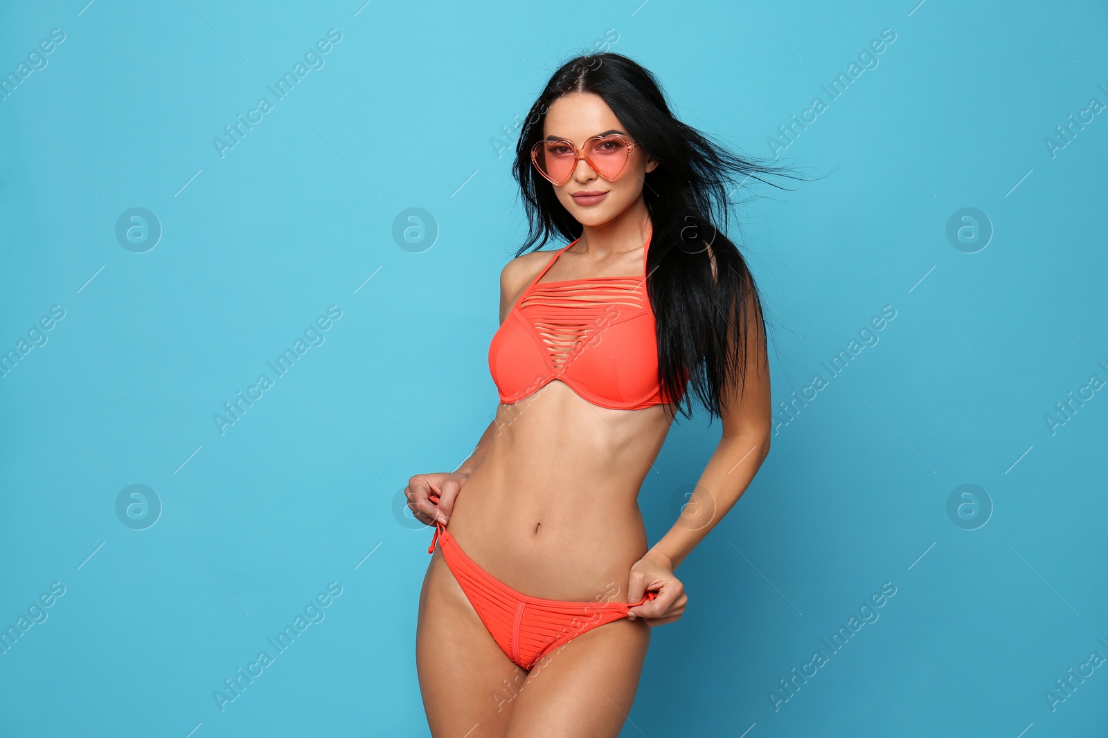 Photo of Beautiful young woman in stylish bikini with sunglasses on light blue background