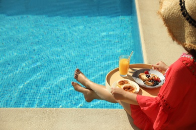 Photo of Young woman with delicious breakfast on tray near swimming pool, closeup. Space for text