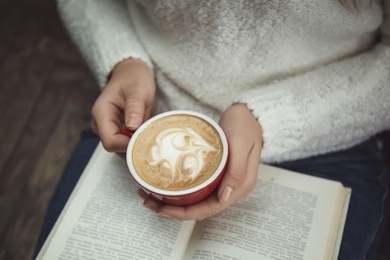 Woman with cup of coffee reading book at home, closeup