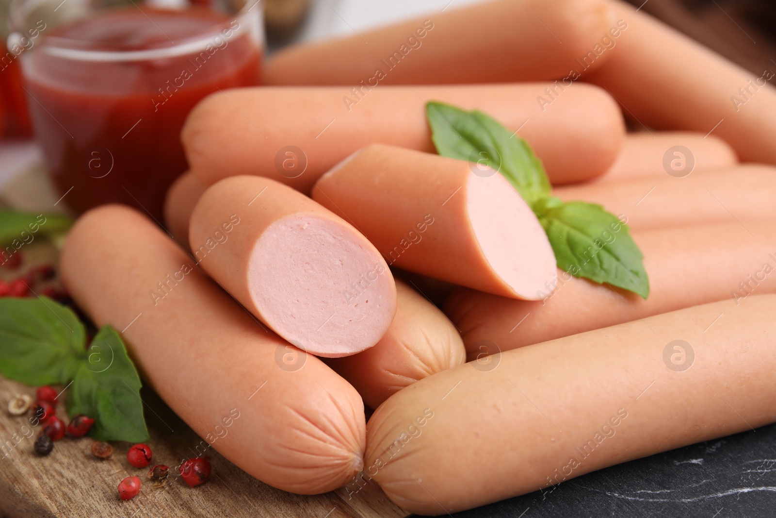 Photo of Delicious boiled sausages, basil and peppercorns on table, closeup