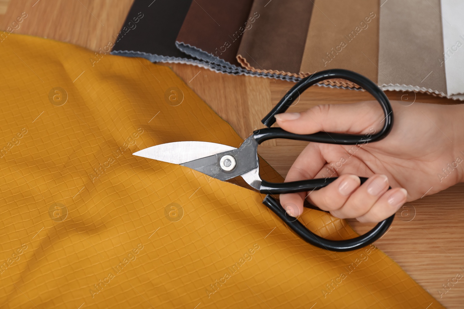 Photo of Woman cutting orange leather with scissors at wooden table, closeup