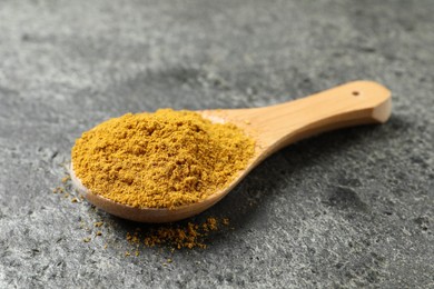 Photo of Spoon with dry curry powder on dark textured table, closeup