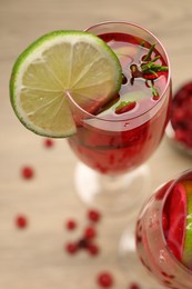 Tasty cranberry cocktail with rosemary and lime in glasses on beige table, closeup