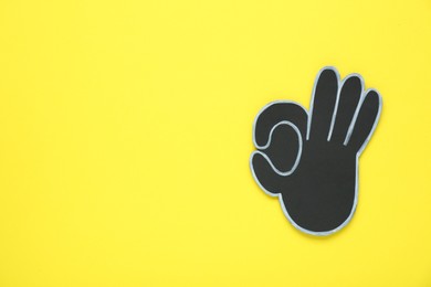 Photo of Paper cutout of okay hand gesture on yellow background, top view. Space for text