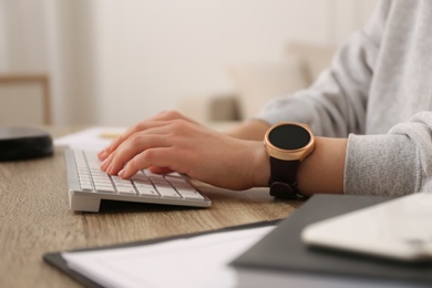 Photo of Young woman with smart watch working at table in office, closeup