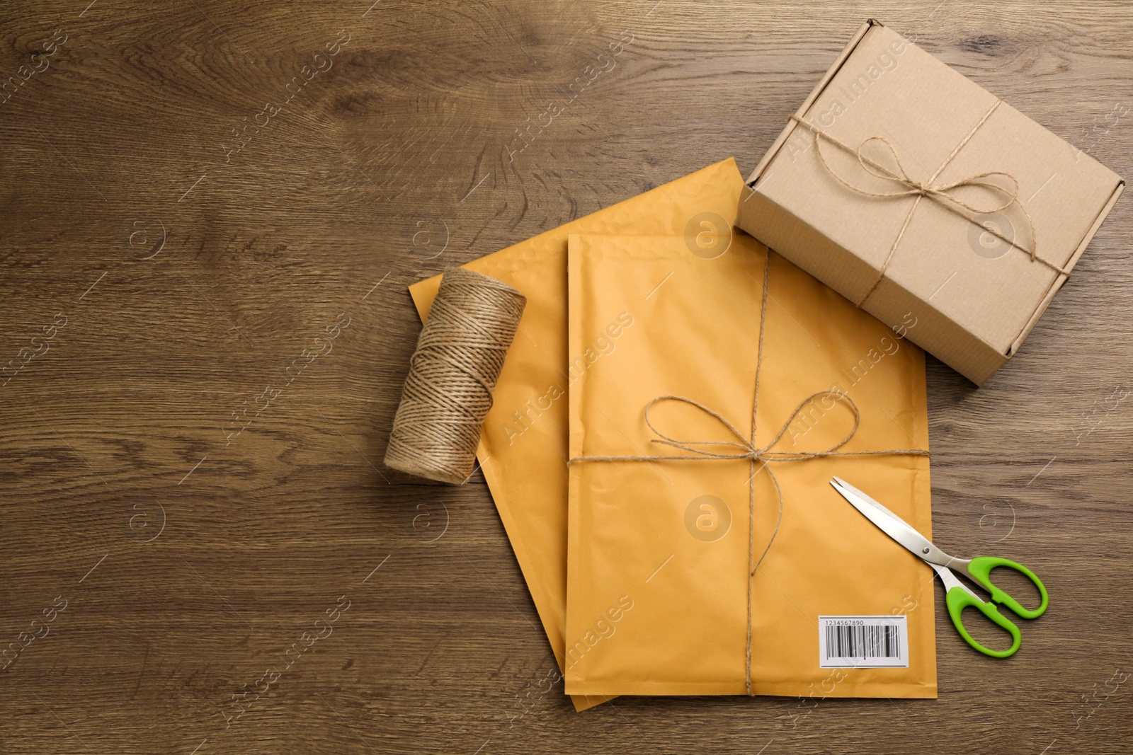 Photo of Padded envelopes, box, rope and scissors on wooden background, flat lay. Space for text