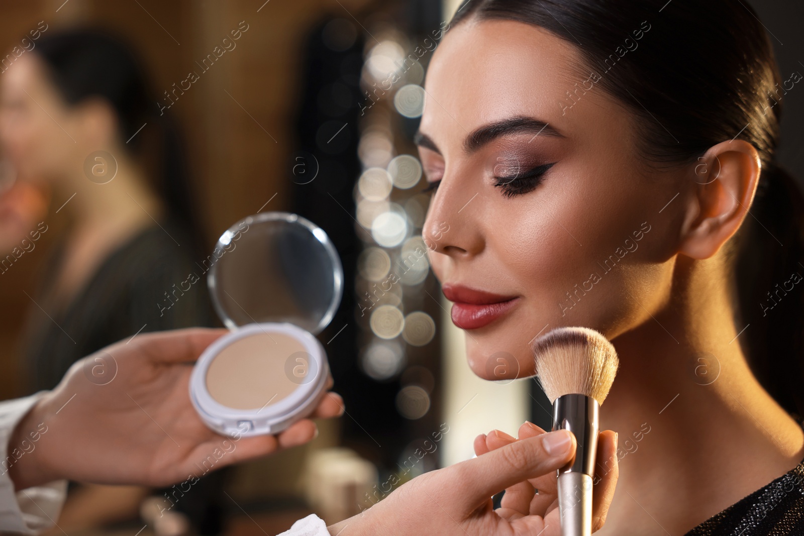 Photo of Makeup artist working with beautiful woman in dressing room, closeup