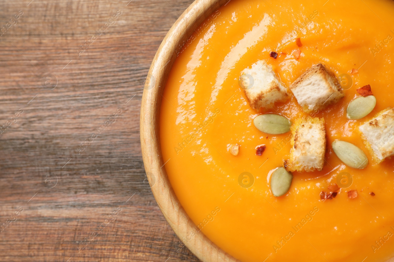 Photo of Bowl with tasty pumpkin cream soup on wooden table, top view. Space for text