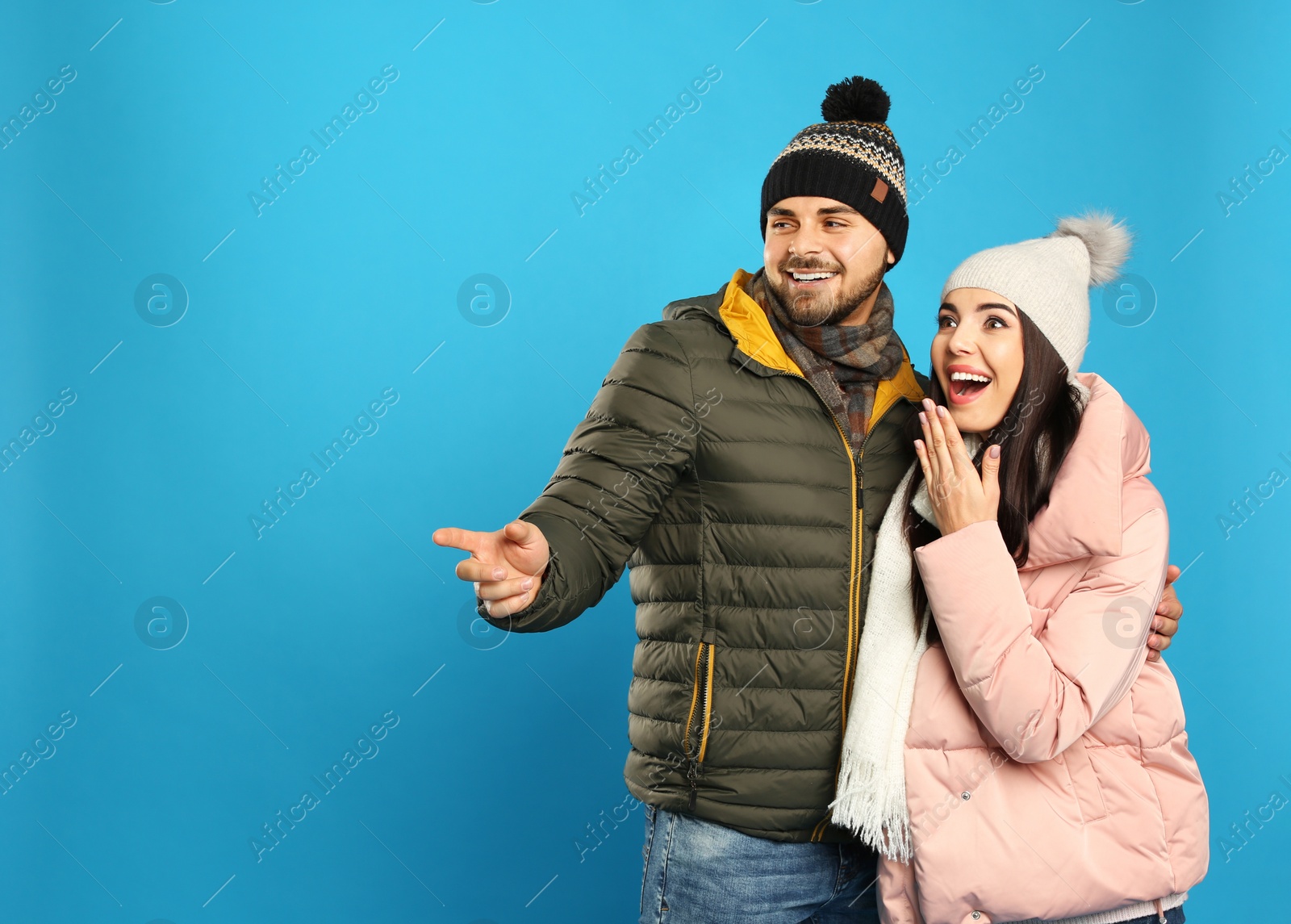 Photo of Happy young couple in warm clothes on blue background, space for text. Winter vacation