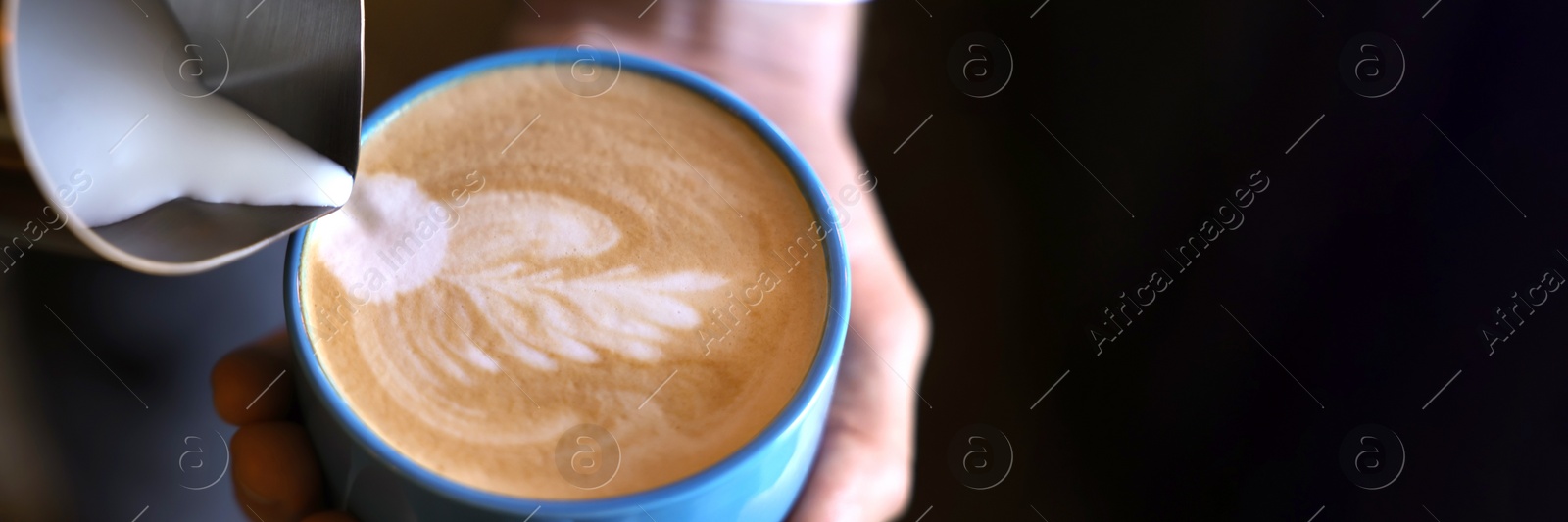 Image of Barista pouring milk into cup of coffee on black background, closeup view with space for text. Banner design