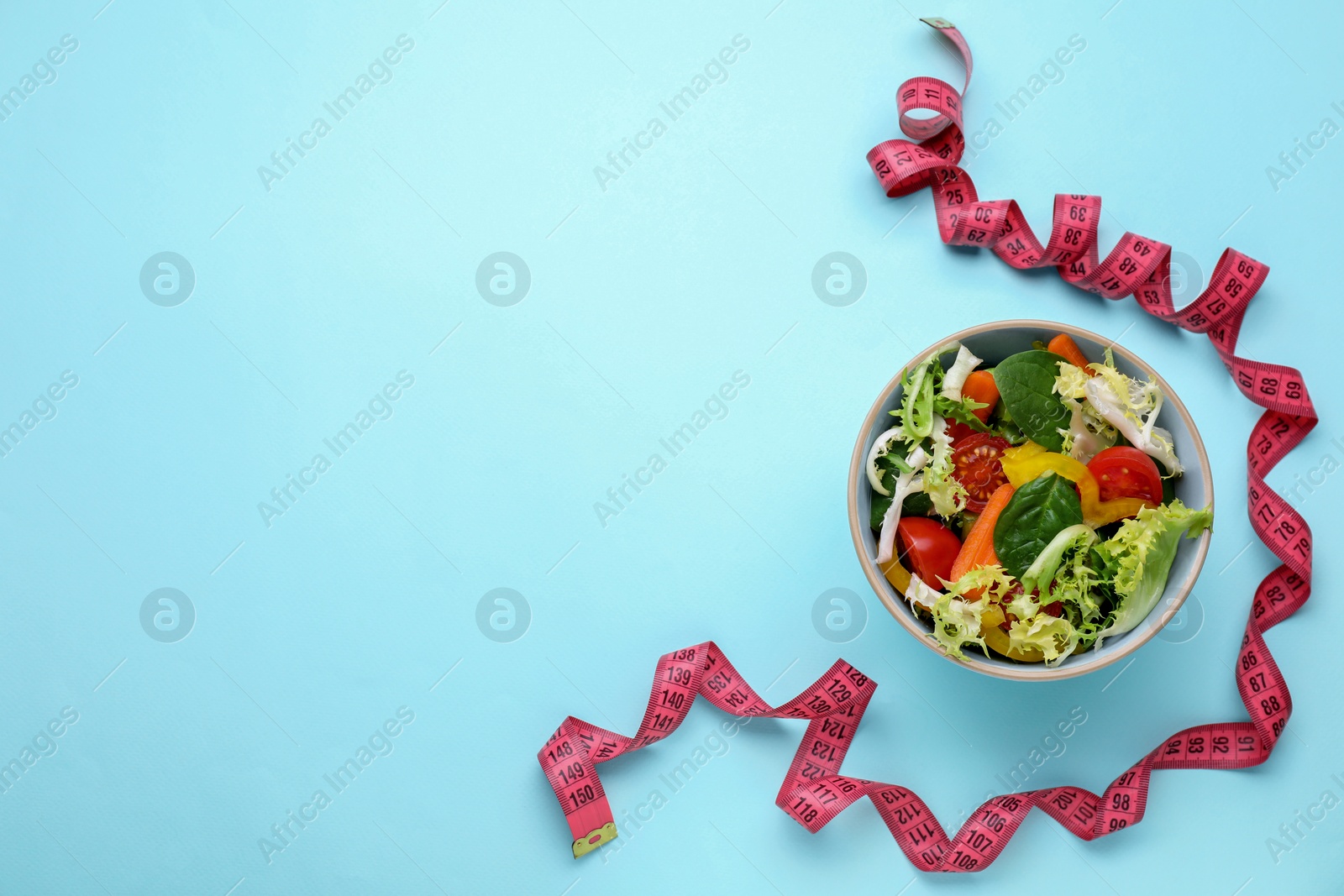 Photo of Measuring tape and salad on light blue background, flat lay. Space for text