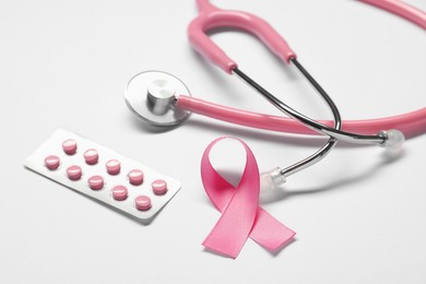 Photo of Pink ribbon, stethoscope and pills on white background, closeup. Breast cancer awareness