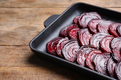 Baking dish with roasted beetroot slices on wooden table, closeup