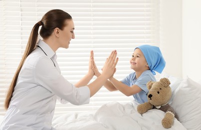 Childhood cancer. Doctor and little patient playing clapping game with hands in hospital