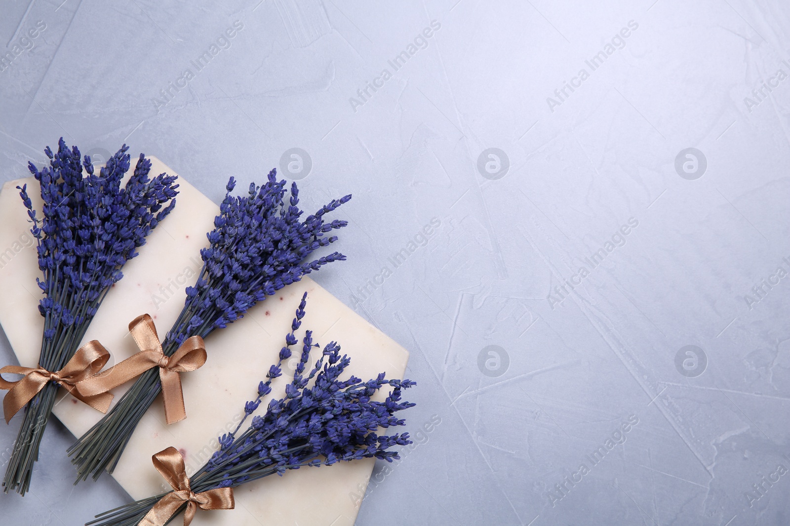 Photo of Bouquets of beautiful preserved lavender flowers and stone board on light grey textured table, top view. Space for text