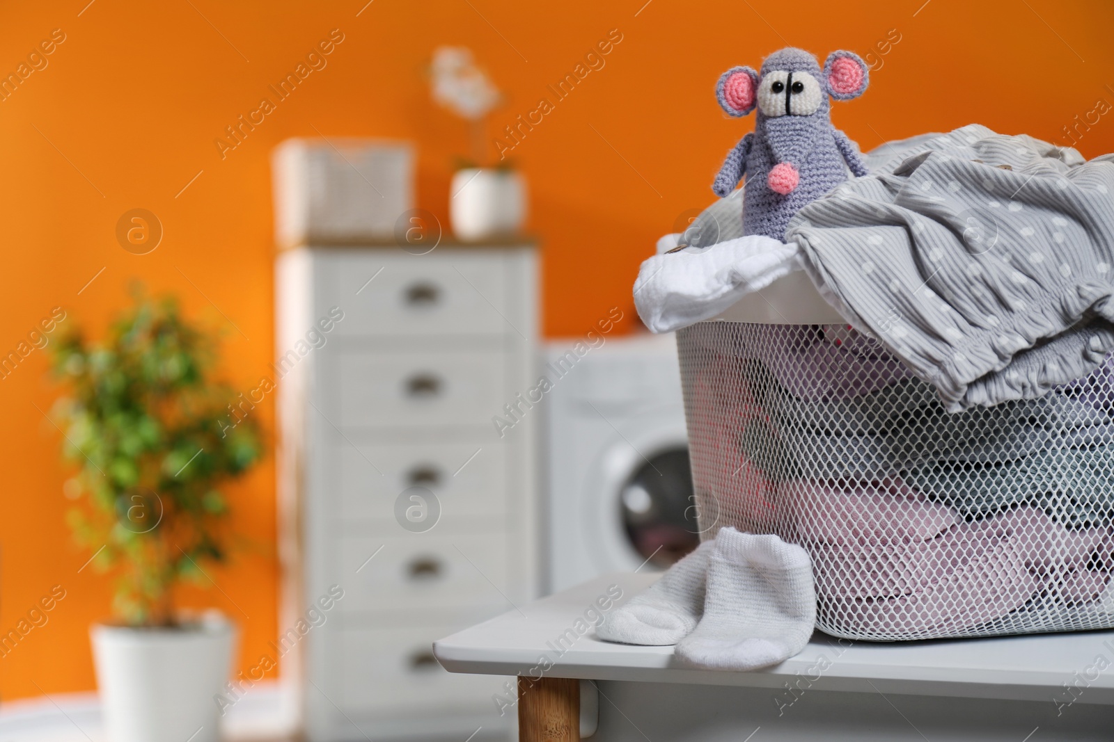 Photo of Laundry basket with baby clothes and toy on table in bathroom, closeup. Space for text